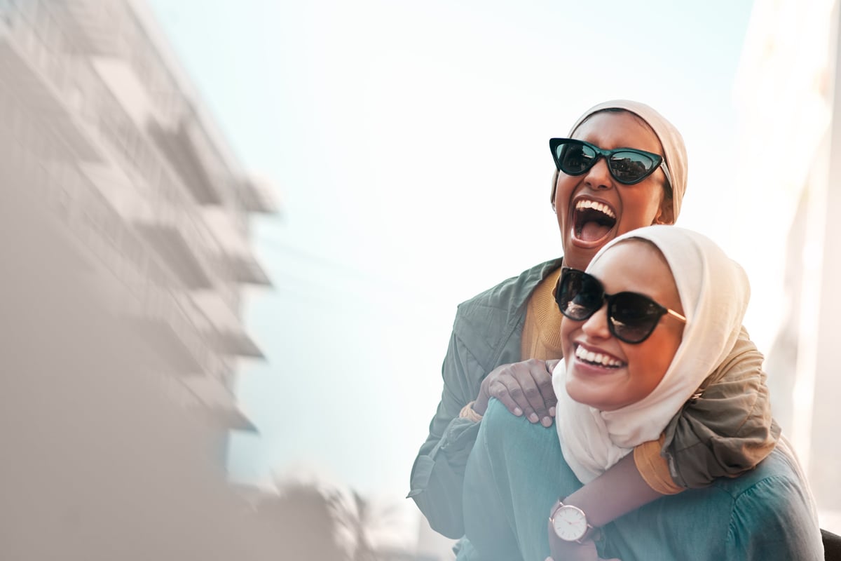 A joyful woman in a headscarf giving her friend a piggyback ride