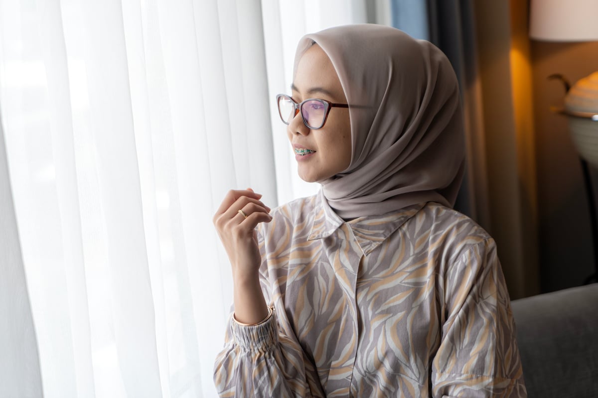 A woman in hijab smiling while looking out a bright window