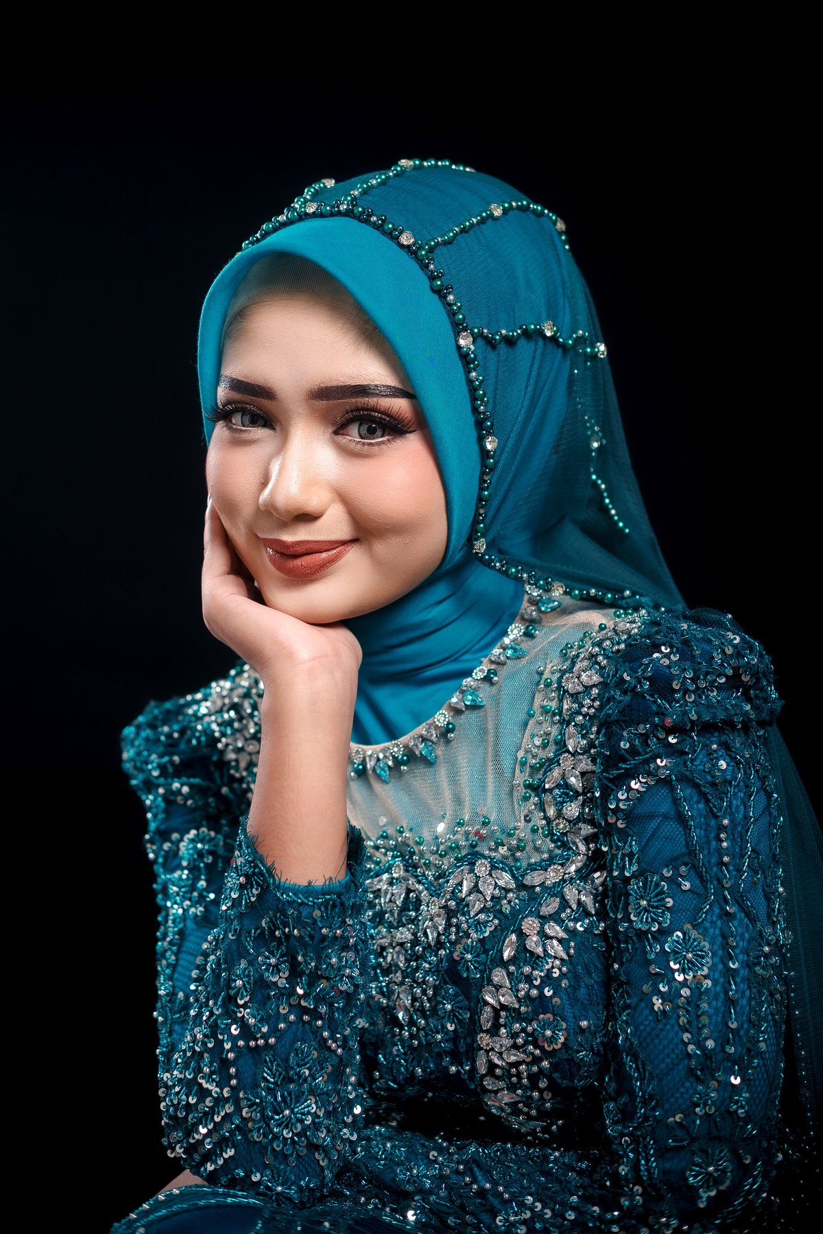A woman in an embellished turquoise hijab, smiling softly